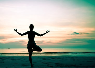 Silhouette of person in yoga tree pose on the beach