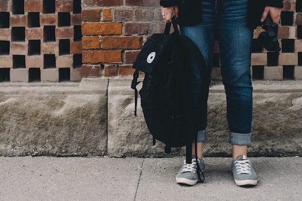 image of child's legs standing next to a wall holding back pack